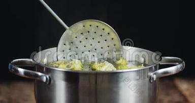 从锅里拿出一个开槽勺子准备西兰花。